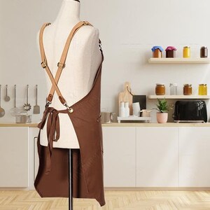 May include: Brown leather-trimmed apron with adjustable straps. The apron is made of a durable canvas material and has a large pocket on the front.
