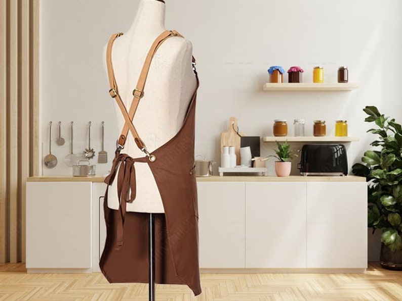 May include: Brown leather-trimmed apron with adjustable straps. The apron is made of a durable canvas material and has a large pocket on the front.