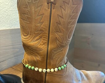 May include: Brown leather cowboy boot with a green and white beaded ankle bracelet.