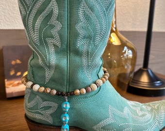 May include: A pair of turquoise cowboy boots with white stitching and a beaded ankle bracelet with turquoise skull charms.