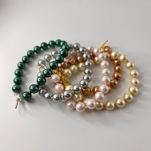 May include: Four pearl bracelets in different colors: dark green, silver, light brown, and white. The bracelets are made of round pearls and are stacked on top of each other.