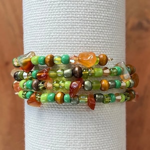May include: Multi-strand bracelet with green, brown, and orange beads. The bracelet is made with a variety of materials, including glass, wood, and metal.