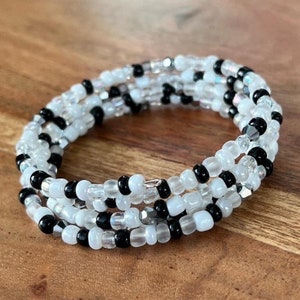 Op de afbeelding: Een meerstrengige armband gemaakt van zwarte en witte kralen. De armband is om zichzelf gewikkeld en ligt op een houten oppervlak.