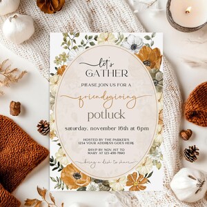 May include: A fall-themed invitation with floral accents and the text "Let's Gather" and "friendsgiving potluck". The invitation is surrounded by autumn decor, including pumpkins, pinecones, and a lit candle.
