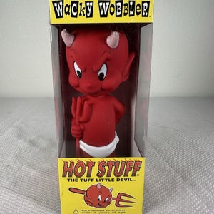 May include: A red Hot Stuff bobblehead figure with small horns and a white diaper, holding a red trident. The figure is inside a yellow and black box labeled Wacky Wobbler and Hot Stuff The Tuff Little Devil with a warning for children under 5.
