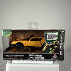 Peut inclure: Une voiture miniature en métal 1977 Chevrolet Camaro Bumblebee dans son emballage d'origine. La boîte présente la marque Transformers Rise of the Beasts, une image du personnage Bumblebee et le texte Voir le robot sur châssis.