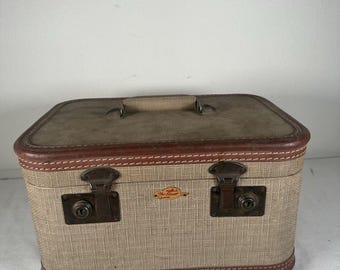 May include: A rectangular beige hard-sided travel case with brown trim and a top handle. The front features two dark metal latches with keyholes and a small gold-toned emblem with the text The Star in red script lettering.