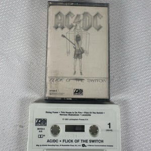 Puede incluir: Una cinta de casete vintage de AC/DC "Flick of the Switch". La caja del casete presenta el logotipo de la banda y la carátula del álbum. La cinta de casete blanca tiene el título del álbum y la lista de canciones impresos.