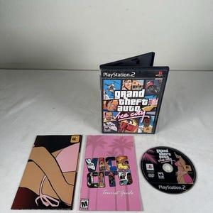 May include: A PlayStation 2 video game case for Grand Theft Auto Vice City, featuring a multi-panel cover art. Included are a black game disc with a character illustration and a pink Vice City Tourist Guide booklet with palm tree graphics.