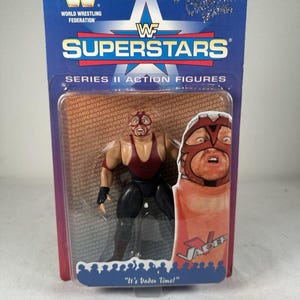 以下が含まれることがあります： ブリスターパックに入ったWWFスーパースターズシリーズIIのベイダーのアクションフィギュア。フィギュアはマルーン色のシングレットと黒いパンツを着用しています。パッケージには「SUPERSTARS」、「SERIES II ACTION FIGURES」、「VADER」、「It's Vader Time!」という文字が記載されています。