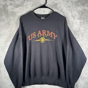 May include: Black crewneck sweatshirt with the text "US ARMY FT DIX" in red and gold lettering. The sweatshirt features a gold emblem below the text. The garment is hanging on a black hanger against a gray background.