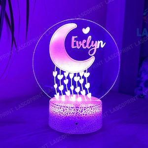 May include: A white acrylic night light with a pink crescent moon and white hearts. The moon has the name "Evelyn" written on it.