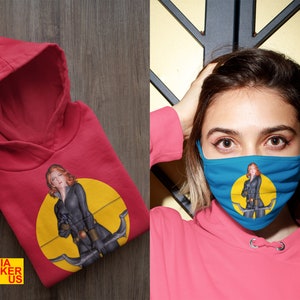 May include: Red hooded sweatshirt with a graphic of a woman in a black outfit holding a bow and arrow. The graphic is on a yellow circle with a black outline.