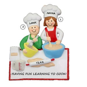 May include: A decorative figurine of two chefs, one named Liam and the other Nana, wearing chef hats and aprons. They are depicted mixing ingredients in bowls, with a rolling pin and the text "HAVING FUN LEARNING TO COOK!" on the base.