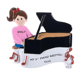 May include: A decorative ornament featuring a figure playing a black grand piano. The figure wears a pink shirt with the name "EMILY" and blue pants. The ornament includes a banner that reads "MY 1ST PIANO RECITAL! YEAR" with musical notes.