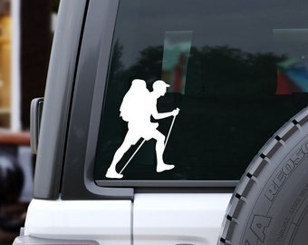May include: White silhouette of a person hiking with a backpack and trekking poles on a car window.
