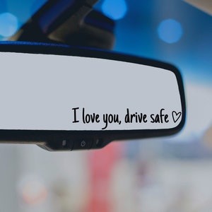 May include: A rearview mirror with the message "I love you, drive safe" written on it in black marker with a small heart drawn next to the text.