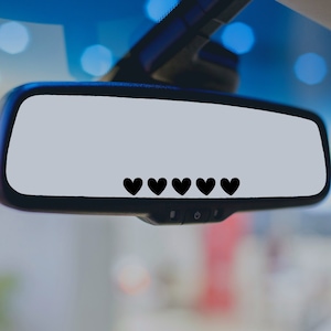 May include: A black rearview mirror with five black hearts in a row across the bottom of the mirror.