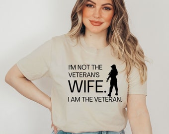 May include: A beige t-shirt with a black graphic that reads "I'm not the veteran's wife. I am the veteran." and a silhouette of a woman holding a rifle.