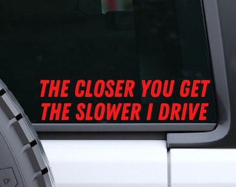 May include: A white car with a red vinyl sticker on the back window that reads "The closer you get the slower I drive."