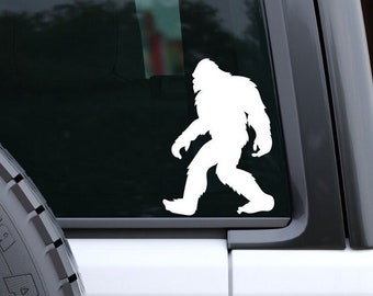 May include: White vinyl sticker of a Bigfoot silhouette walking on a black car window.