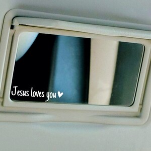 May include: A white car visor with a small mirror that says "Jesus loves you" with a heart symbol.