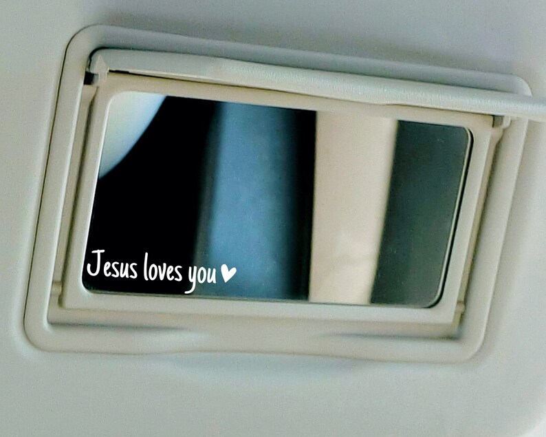 May include: A white car visor with a small mirror that says "Jesus loves you" with a heart symbol.