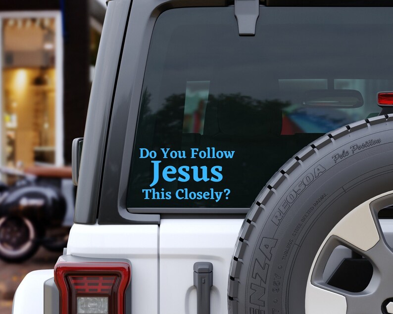 May include: A white Jeep with a blue and white sticker on the back window that reads "Do You Follow Jesus This Closely?"