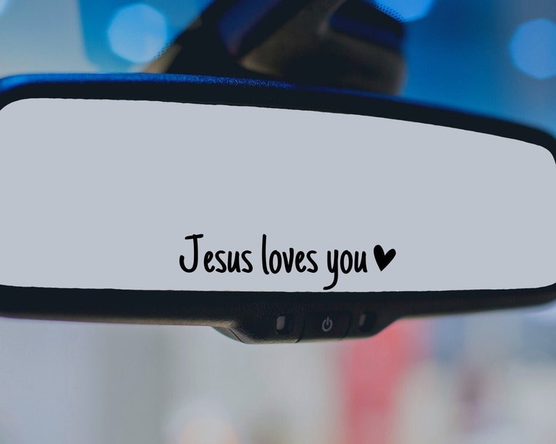 May include: A rearview mirror with the text "Jesus loves you" and a heart symbol written on it.