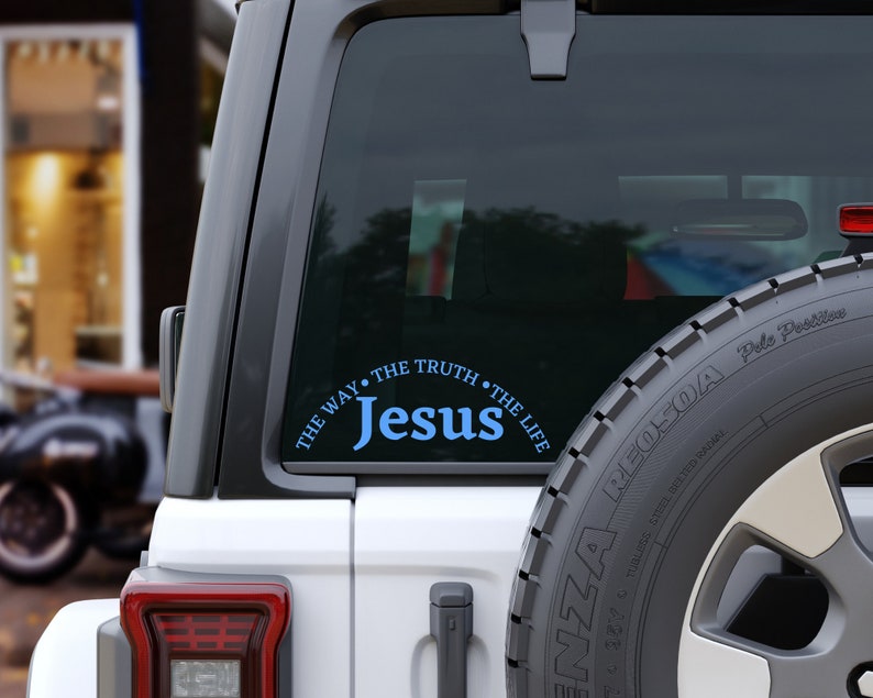Puede incluir: Un coche blanco con una pegatina azul y blanca en la ventana trasera que dice "Jes&uacute;s, El Camino, La Verdad, La Vida".