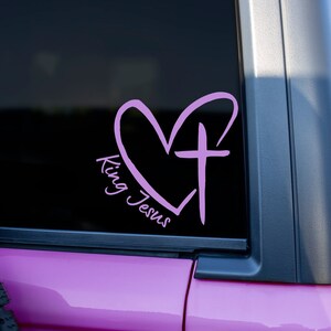 May include: Pink vinyl decal with a heart and cross design. The text "King Jesus" is written in a cursive font.