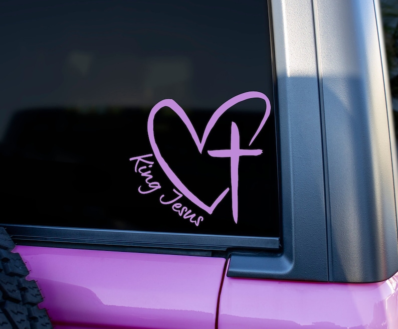 May include: Pink vinyl decal with a heart and cross design. The text "King Jesus" is written in a cursive font.