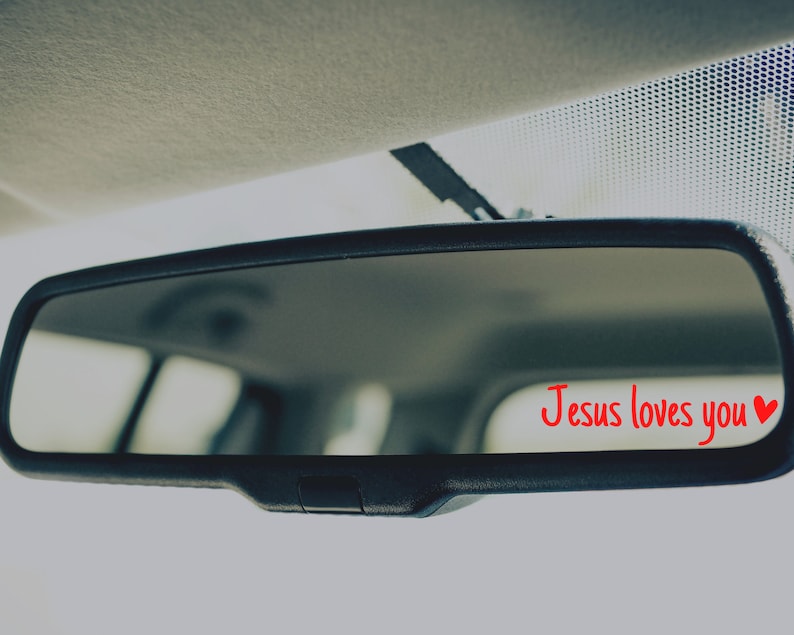 May include: A rearview mirror with the words "Jesus loves you" and a red heart written on it in red.