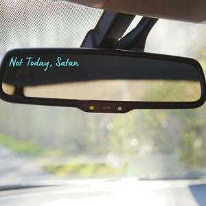 May include: A rearview mirror in a car with the text "Not Today, Satan" written on it in turquoise.