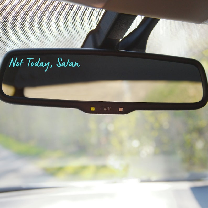 May include: A rearview mirror in a car with the text "Not Today, Satan" written on it in turquoise.