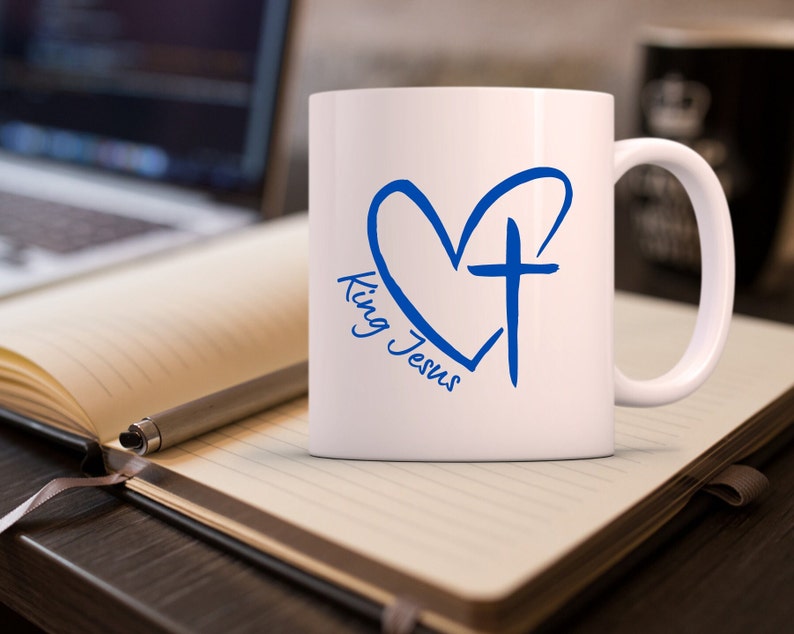 May include: White ceramic mug with a blue heart and cross design. The text "King Jesus" is written inside the heart.