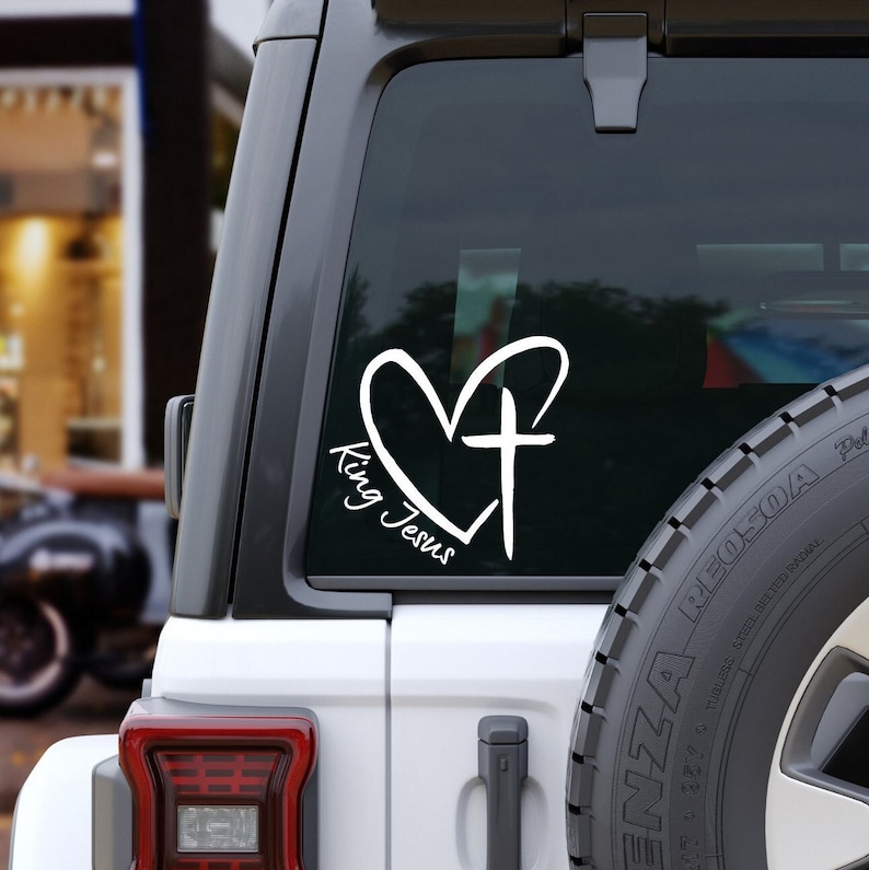 May include: White vinyl decal with a heart and cross design. The text "King Jesus" is written inside the heart.