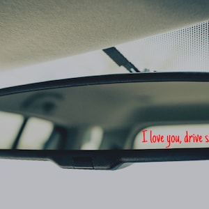 May include: A rearview mirror with the message "I love you, drive safe" written in red on the glass.