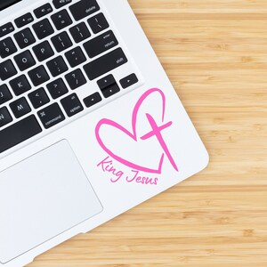 May include: A white laptop with a pink heart and cross design sticker that says "King Jesus".