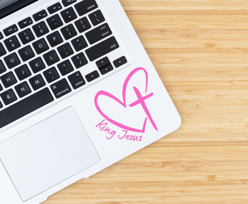 May include: A white laptop with a pink heart and cross design sticker that says "King Jesus".