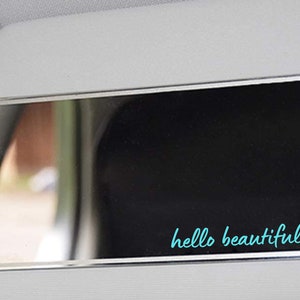 May include: A silver car visor mirror with a black background and the text "hello beautiful" in turquoise with a turquoise heart.