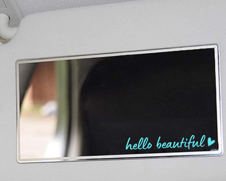 May include: A silver car visor mirror with a black background and the text "hello beautiful" in turquoise with a turquoise heart.