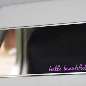 May include: A silver car visor mirror with a black background and the text "hello beautiful" in purple with a pink heart.