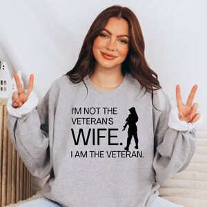 May include: Grey sweatshirt with the text "I'm not the veteran's wife. I am the veteran." and a silhouette of a woman in military uniform.