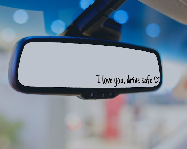 May include: A rearview mirror with the message "I love you, drive safe" written on it in black marker with a small heart drawn next to the text.