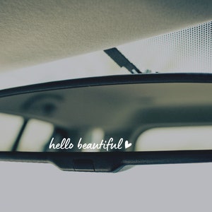 May include: A rearview mirror with the text "hello beautiful" and a small heart symbol written on the reflective surface.