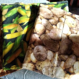 May include: A collection of fabric items with various food-themed patterns. One features corn on a dark background, while others display potato and stone designs. The items appear to be folded, showcasing the different patterns.