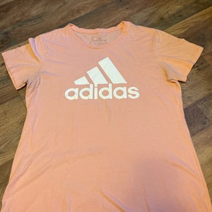 May include: A pink t-shirt with a white Adidas logo.