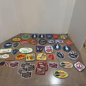 May include: A collection of various embroidered bowling patches featuring diverse shapes and colors. The patches display text such as WIBC, WBA, League Champion, and All Spare Game, along with graphics of bowling pins, balls, and maps of Kentucky.