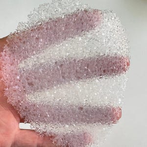 以下が含まれることがあります： 透明で白く、質感があり、わずかに半透明なシート状の素材のクローズアップ。素材は半分に折り畳まれており、薄くて柔軟なプラスチックでできているようです。